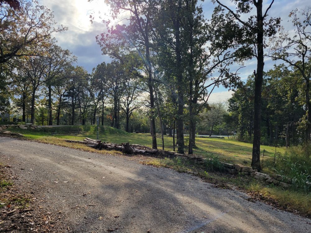 A gravel park road edged with natural stone borders and shade trees in afternoon sunlight.