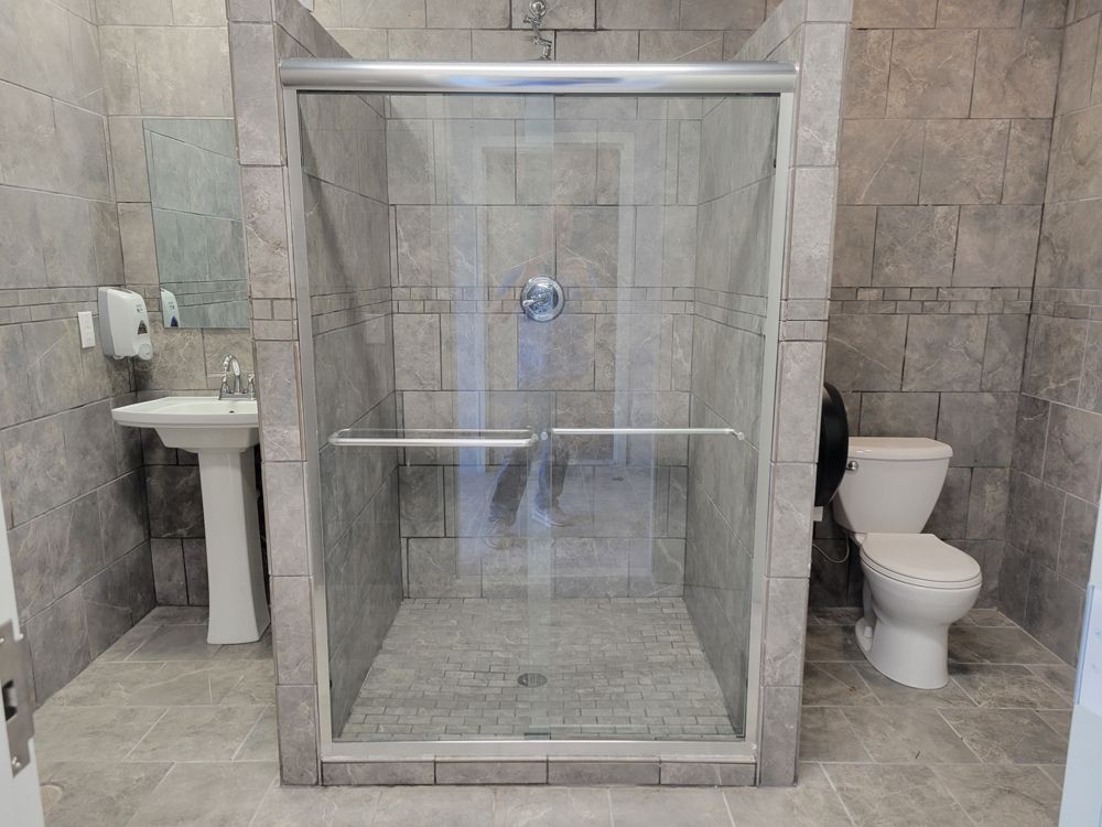 A clean, modern tiled bathhouse with a glass-door shower, pedestal sink, and toilet.